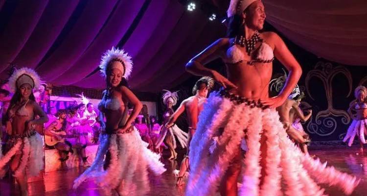 Traditionelle polynesische Tänzer in gefiederten Kostümen, die nachts auf einer beleuchteten Bühne auftreten.