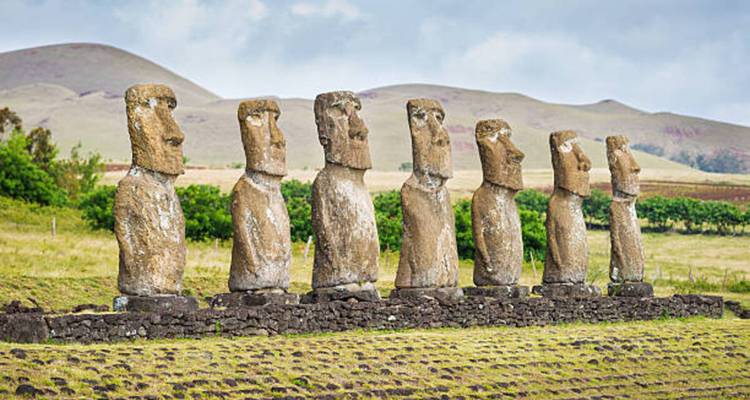 Sieben aufrecht stehende Moai-Statuen von Ahu Akivi auf einer Steinplattform vor hügeligen Hügeln angeordnet.