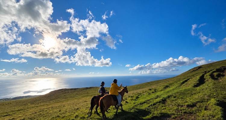 Zwei Reiter zu Pferd, die einen grasbewachsenen Bergrücken durchqueren, mit weiter Aussicht auf den Pazifik unter klarem Himmel.