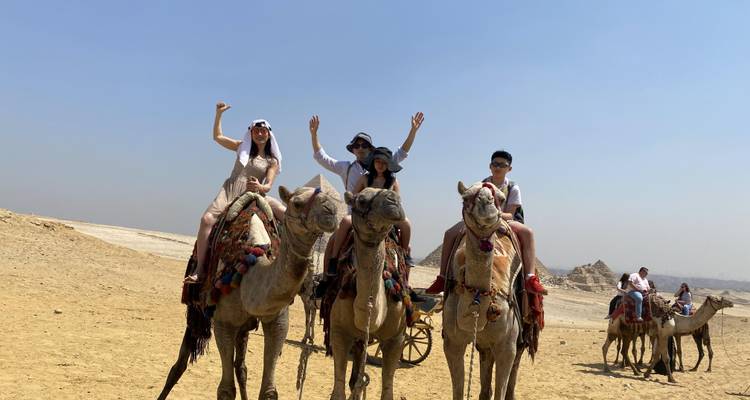 Groupe de personnes montant des chameaux dans un paysage désertique avec des pyramides en arrière-plan.