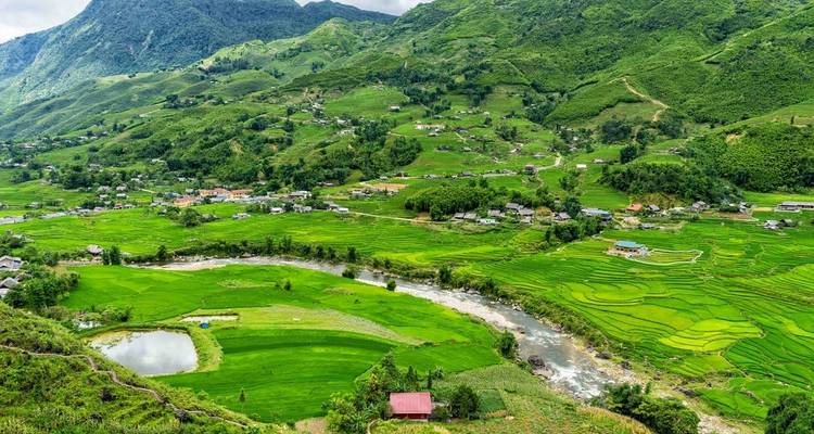 Amplia vista panorámica de exuberantes valles verdes en terrazas y un río serpenteante ubicado entre montañas brumosas.