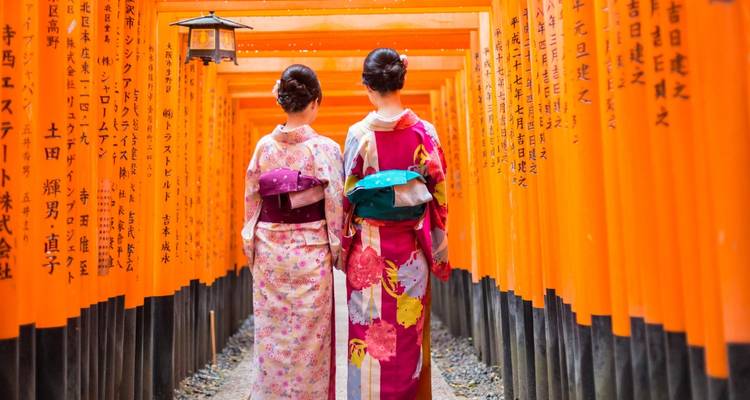Deux femmes en kimonos colorés marchent à travers les innombrables portiques torii orange du sanctuaire Fushimi Inari