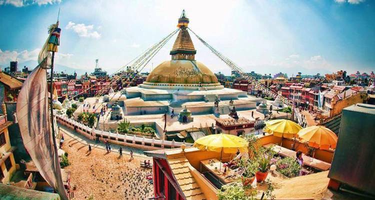 Een grote stupa omringd door kleurrijke gebouwen en gebedsvlaggen onder een blauwe hemel.