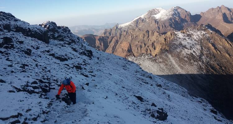 Una persona escalando una montaña cubierta de nieve con una amplia vista de los picos.