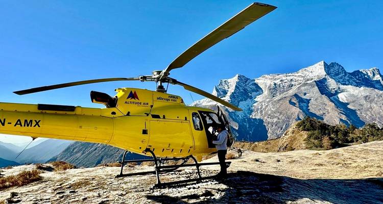 Yellow helicopter on the ground with snowy mountains in the background.