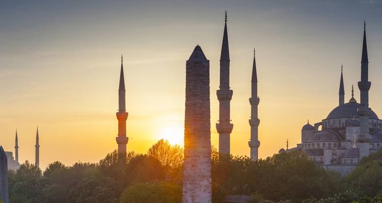 Silhouette of a mosque and obelisk against the sunset.