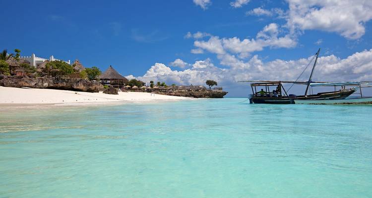 Lagon turquoise cristallin et plage de sable blanc avec un dhow ancré au large à Zanzibar.
