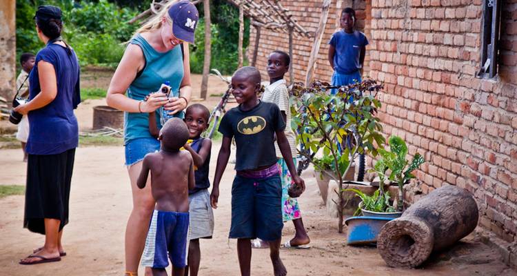 Un voyageur rit avec des enfants locaux devant des maisons en brique dans un village rural.