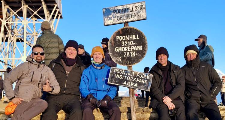 Grupo de excursionistas posando en un mirador con señalización que indica Poon Hill.
