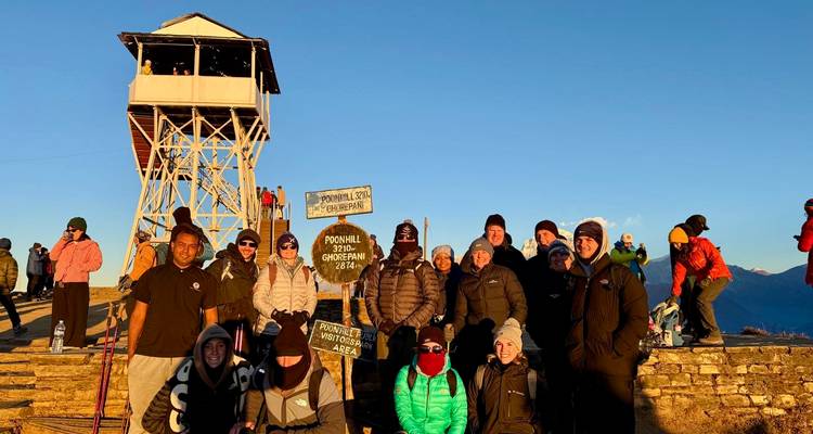 Gran grupo de excursionistas posando con carteles que indican el mirador de Poon Hill.