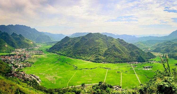 Elevated panoramic view over a broad green valley surrounded by karst mountains and scattered villages.