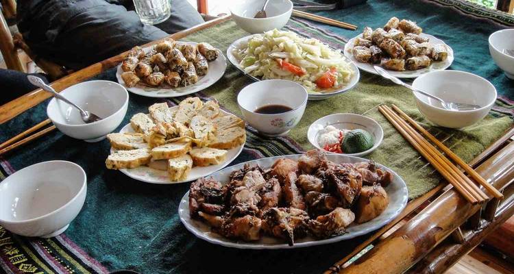 Plates of grilled pork, spring rolls, pickled vegetables and dipping sauces arranged on a bamboo table