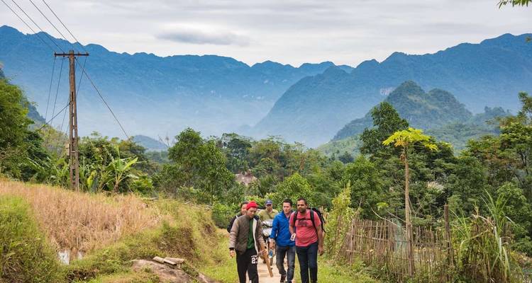 Group of trekkers walking on a dirt path through rural farmland with mountains in the distance