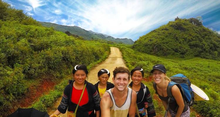 Cheerful selfie of travellers with local guides on a lush mountain trail under a bright sky