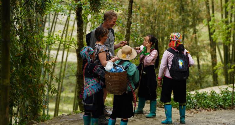 Traveller chats with local ethnic minority women in colourful attire along a forest path.