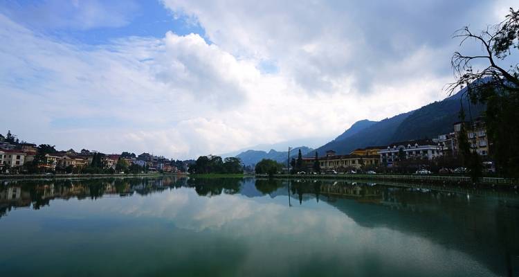 Calm mountain town reflected in a still lake under a partly cloudy sky.