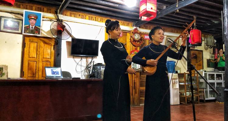 Dos mujeres en vestimenta tradicional interpretando música con un laúd dentro de un salón comunitario