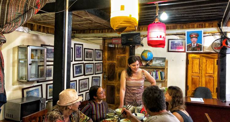Travelers chatting and eating in a cozy, photo-lined homestay dining room
