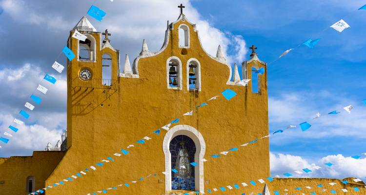 Una iglesia amarilla con banderas y un cielo azul.