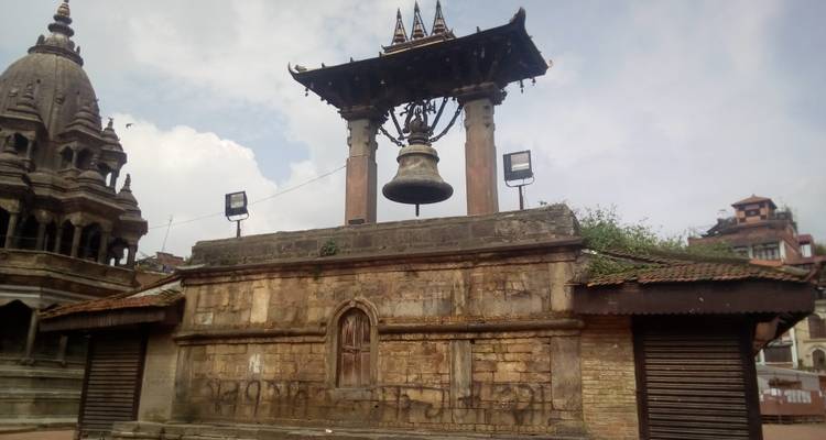 A large traditional bell on a stone platform with nearby historical structures.