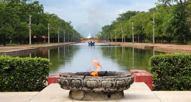 A sacred flame burning by a reflective pond with a distant stupa.