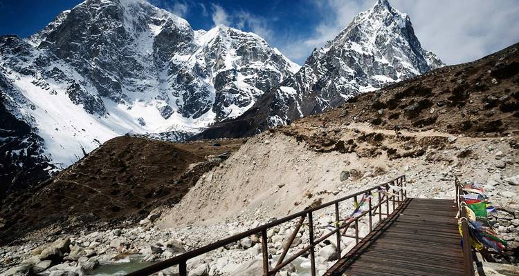 Holzbrücke über einen Fluss mit schneebedeckten Bergen.