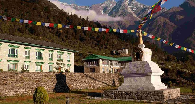 Buddhistische Stupa mit Gebetsfahnen und Bergen im Hintergrund.