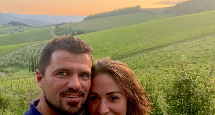 Couple posant avec des vignobles en arrière-plan au coucher du soleil.