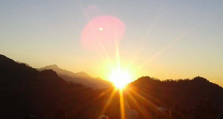 Sunset over mountain landscape with sun rays visible.