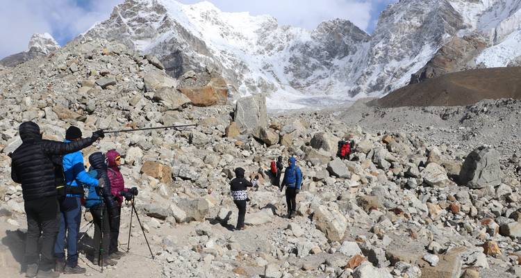 Trekkers con cámaras explorando la morrena rocosa bajo la cresta nevada del Himalaya.