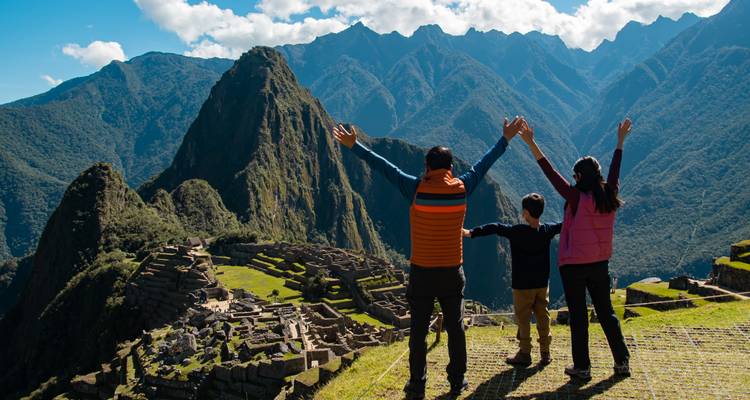 Padres e hijo levantan los brazos en triunfo en la terraza con vistas a las ruinas de Machu Picchu.