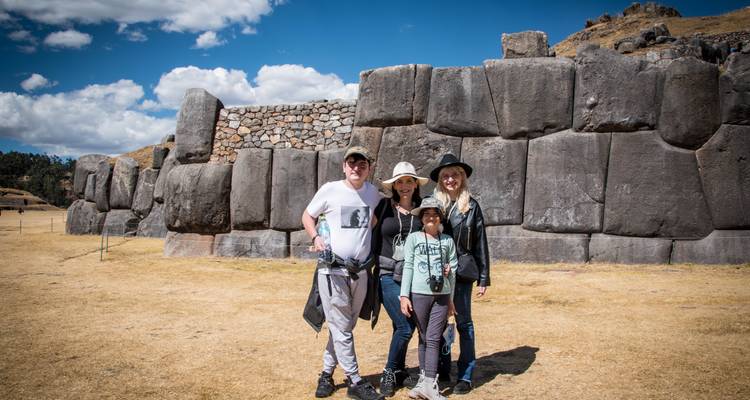 Una familia posa frente a los enormes muros de piedra inca con forma de zigzag en Sacsayhuamán bajo un cielo despejado.