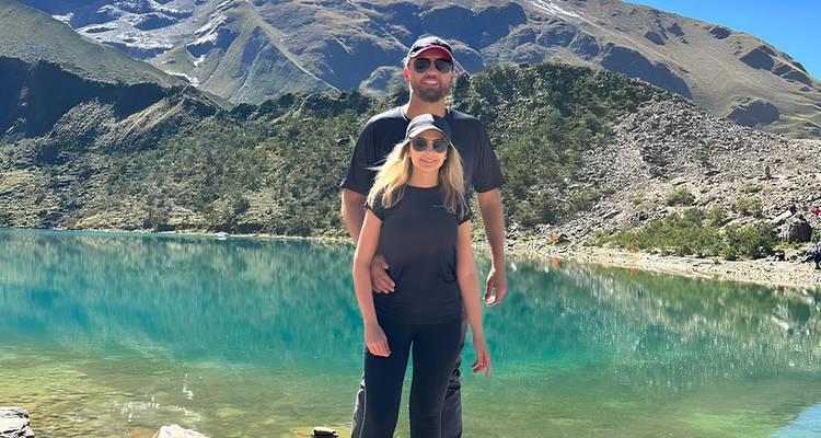 Una pareja frente a un lago de montaña cristalino con montañas rocosas.