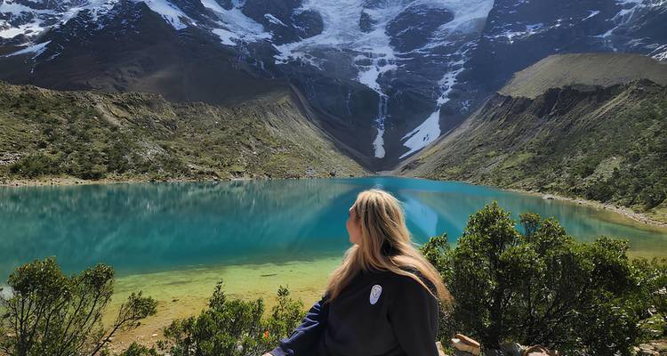 Una mujer mirando un lago turquesa y montañas cubiertas de nieve.