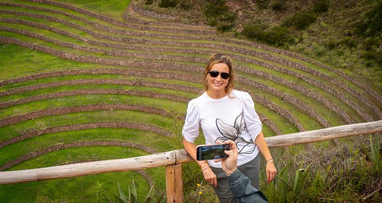 Una mujer posa sobre una barandilla con una vista panorámica de los terrenos agrícolas concéntricos de Moray debajo.