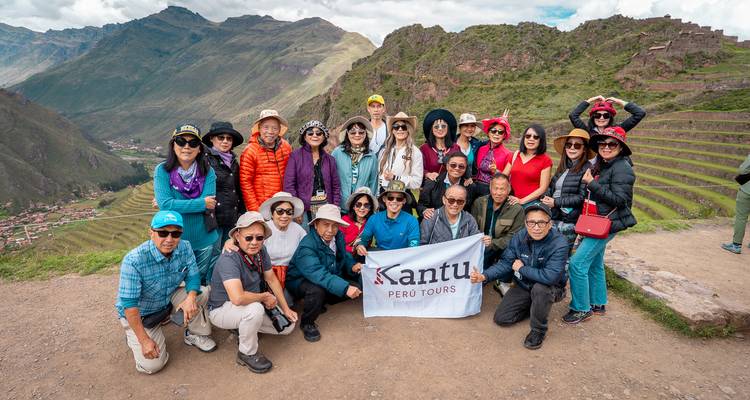 Un gran grupo de turismo muestra la pancarta de la empresa en un mirador sobre las laderas escalonadas de Pisac.