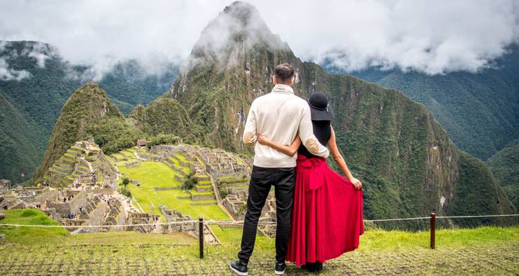 Pareja abrazándose mientras admiran las ruinas de Machu Picchu y el pico de Huayna Picchu envuelto en niebla.
