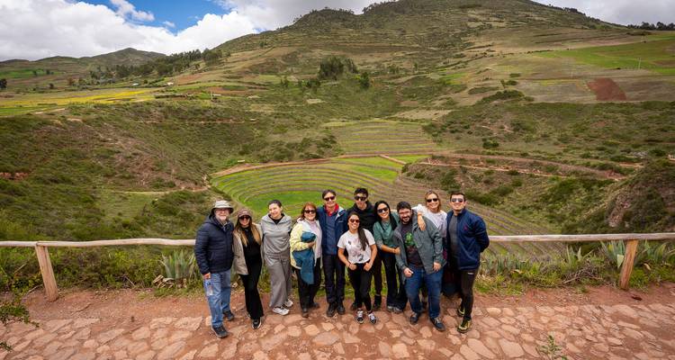 Un grupo grande de turismo de pie en un mirador con vista a los exuberantes campos en terrazas del Valle Sagrado de Perú.