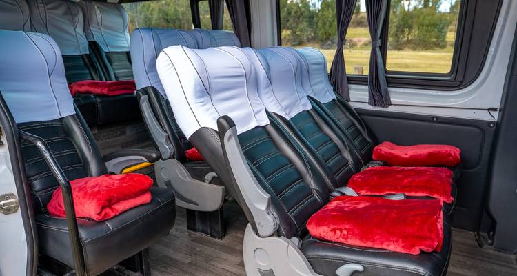 Otro ángulo de los asientos acolchados del minibús con reposacabezas azul-blanco y mantas rojas.