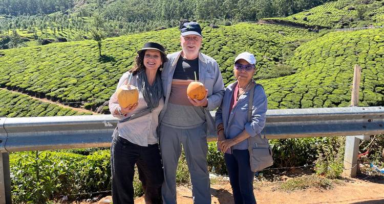 Three travelers smiling with fresh coconuts in front of rolling green tea plantations