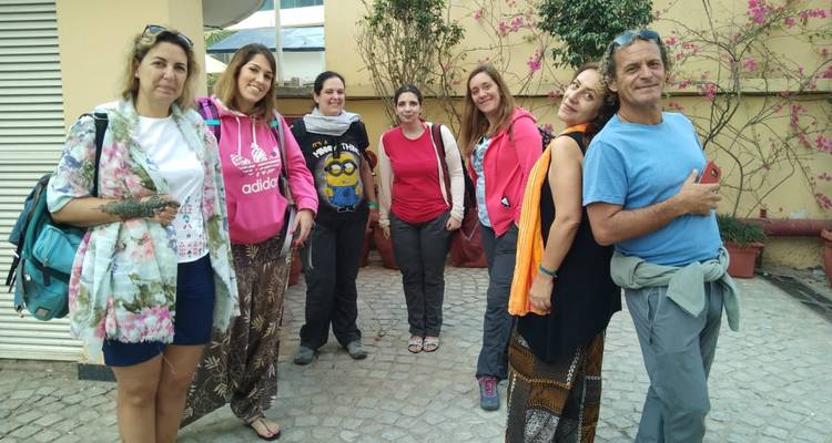 Seven women posing together outside a building, dressed casually for travel