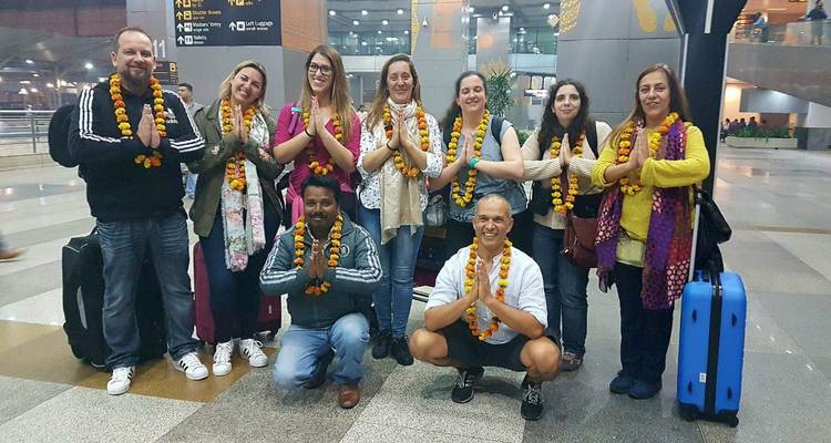 Group of travelers at an airport greeting area wearing flower garlands and posing with hands together