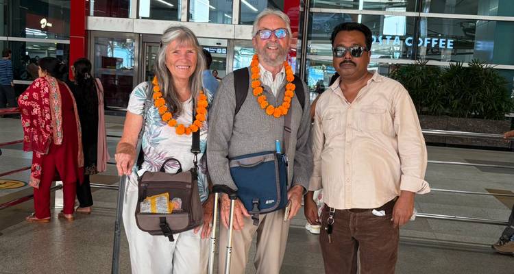Two travelers with marigold garlands and their guide outside an airport terminal