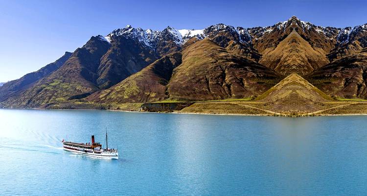 Bateau à vapeur d'époque naviguant sur un lac turquoise sous des montagnes spectaculaires aux sommets enneigés