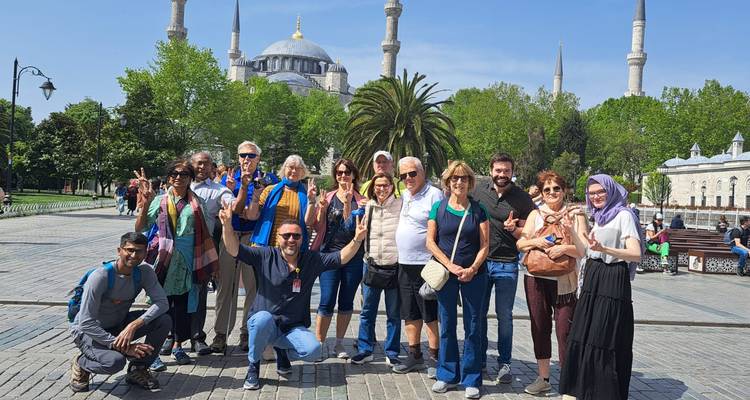 Grupo de viajeros posando frente a la Mezquita Azul con árboles frondosos y un cielo azul brillante.