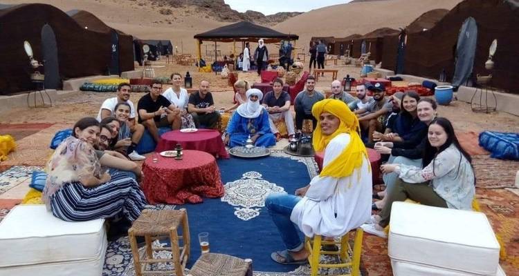 Groep mensen die buiten zitten in traditionele kleding in een woestijnkamp.