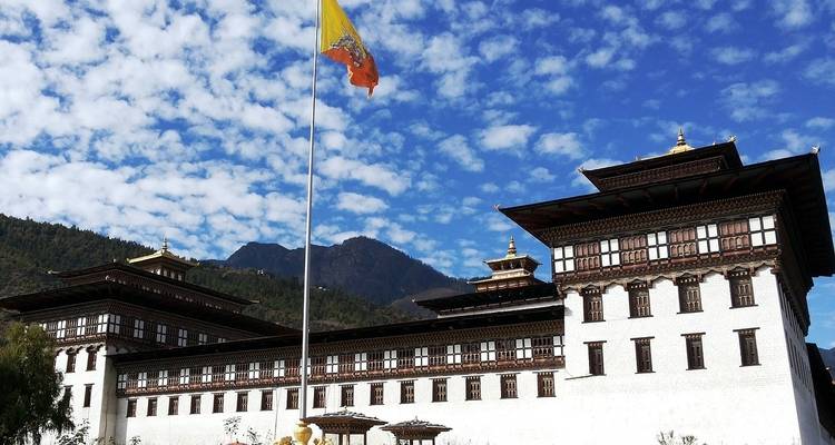 Traditionele Bhutanese architectuur met een vlag en bergachtergrond.