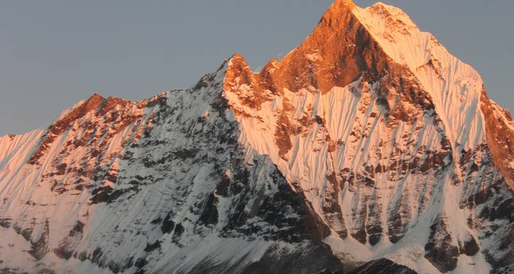 Snow-capped peak of a mountain glowing under the setting sun.