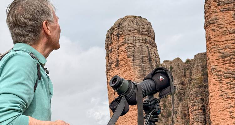 Une personne avec un appareil photo sur un trépied observant de grandes formations rocheuses.