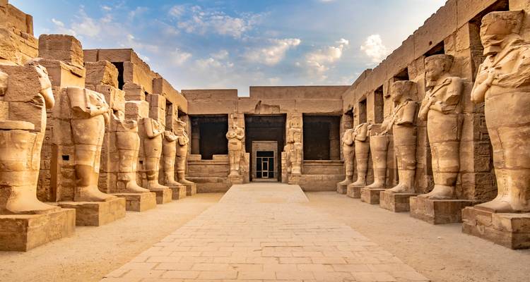 Avenue processionnelle bordée de statues colossales de pharaons à l'intérieur d'un temple égyptien antique au lever du soleil